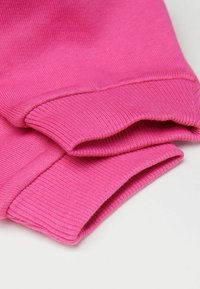 Detail dvou složených růžových ribbed pletených rukávů s viditelným švem na bílém pozadí.