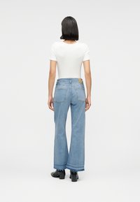 Φόρεμα λευκής εφαρμοστής μπλούζας σε συνδυασμό με ανοιχτό μπλε τζιν παντελόνι με φαρδιά μπατζάκια, με ακατέργαστο τελείωμα και σκούρα ραφή. Μαύρα μποτάκια μέχρι τον αστράγαλο ολοκληρώνουν το σύνολο.