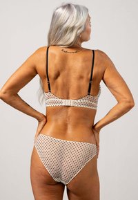 Polka dot bikini set in nude met zwarte stippen. Heeft verstelbare zwarte bandjes en een haaksluiting op de rug. Zachte stoftextuur.