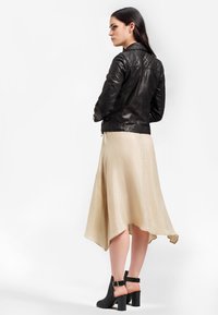 Veste en cuir noir de biker avec des détails matelassés, associée à une jupe midi beige fluide et des bottines noires à talons avec un dos ouvert.