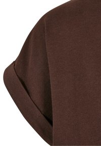 Gros plan d'une manche courte marron avec un revers roulé sur un vêtement en tissu texturé.