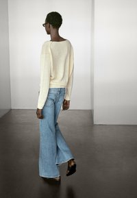 Maglione in maglia beige chiaro con una vestibilità morbida, abbinato a jeans svasati azzurri. Scarpe nere slip-on completano l'outfit.