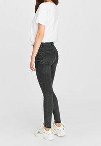 Černé skinny džínsy vyrobené z elastického denimu, s vysokým pasem, zadními kapsami a přiléhavým střihem. V kombinaci s bílými teniskami.