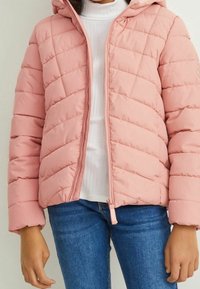Giacca imbottita rosa chiaro con chiusura a zip, cappuccio e design trapuntato. Presenta maniche lunghe e vita aderente, abbinata a una maglietta bianca e jeans.