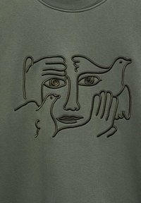 Abstrakcyjny rysunek twarzy wykonany ciągłą linią z rękami i dwoma ptakami, wyszyty czarną nicią na oliwkowozielonym materiale.