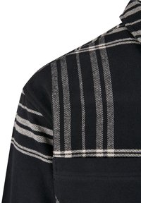 Tissu noir avec motif à carreaux blancs comportant des rayures verticales et horizontales sur l'épaule et la partie supérieure du bras d'une veste.