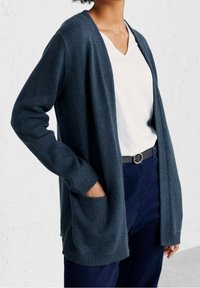 Mörkblå kofta i mjuk stickad kvalitet med relaxed passform, öppen front, ribbad mudd och två framfickor. Bärs över en vit t-shirt med V-urringning.