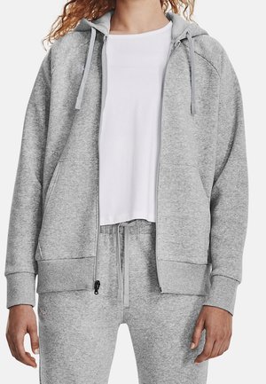 Lichtgrijze zip-up hoodie met een capuchon, voorzakken en trekkoorden. Gemaakt van zacht materiaal met geribbelde manchetten en zoom. Draagt over een wit shirt.