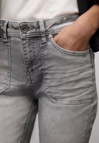 Grijze denim jeans met een klassieke pasvorm, zilverkleurige sluitingen, zichtbare stiksels en twee voorzakken. De stof toont een gladde textuur en subtiele vervaging.