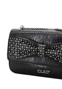 Clutch nero in ecopelle con fiocco decorativo borchiato, dettaglio catena d'argento sulla parte superiore e logo in basso. Finitura testurizzata visibile.
