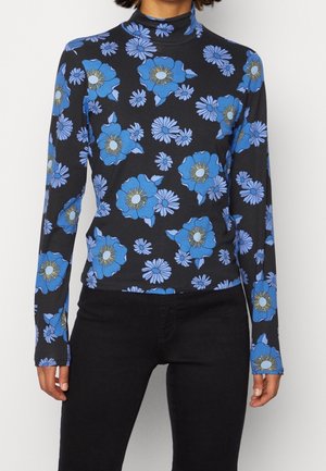 Musta pitkähiuksinen poolopaita, jossa suuri sininen ja vaaleanpunainen kukkaprintti, yhdistetty mustiin housuihin.