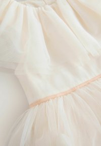 Elfenbeinfarbener Tüllkleid mit geschichteten Rüschen, einem taillierten Oberteil und einem weichen Pfirsichbesatz entlang der Taille, der zarte Texturen hervorhebt.