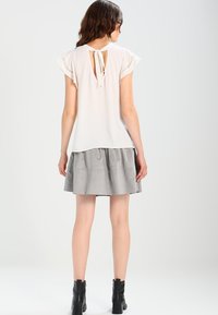 Blusa bianca con maniche corte e volant, con dettagli in pizzo sulle maniche, abbinata a una gonna grigia a campana. Laccio regolabile sul retro.