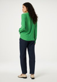 Groene langärmige shirt, lichte stof, met knoopmanschetten, gecombineerd met losse donkere spijkerbroeken en lichte schoenen.