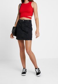 Rode geribbelde crop top gecombineerd met een zwarte denim rok met voorzakken en een hoge taille. G gedragen met zwart-witte sneakers.