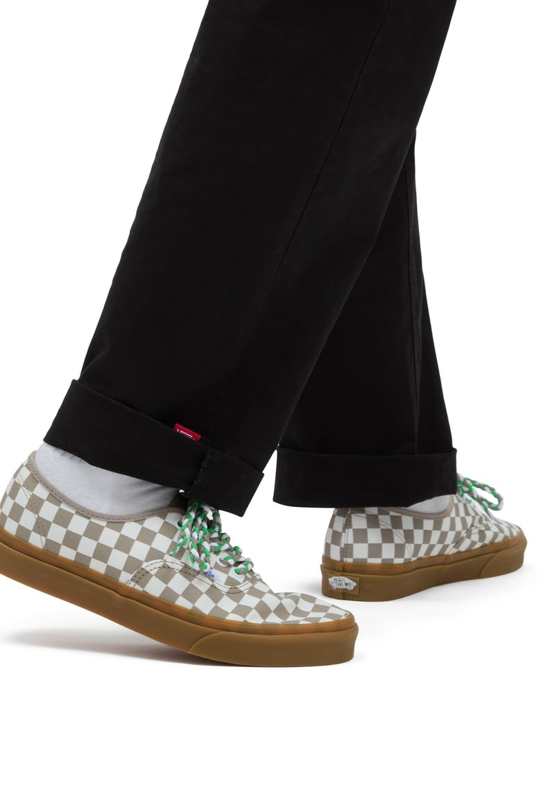 Sneaker di tela a scacchi grigi e bianchi con lacci verdi e bianchi, abbinate a pantaloni neri, che mostrano un design a bassa altezza e suola in gomma.