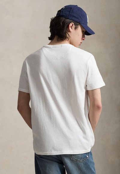 T-shirt en coton blanc avec un col rond classique, manches courtes, texture douce, accompagné d'une casquette bleue et d'un jean en denim, vu de dos.