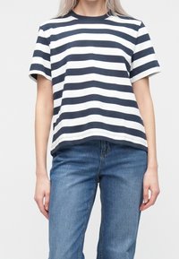 Camiseta de manga corta a rayas azul marino y blancas con cuello redondo; tela de algodón suave; combinada con vaqueros azules de pierna recta.