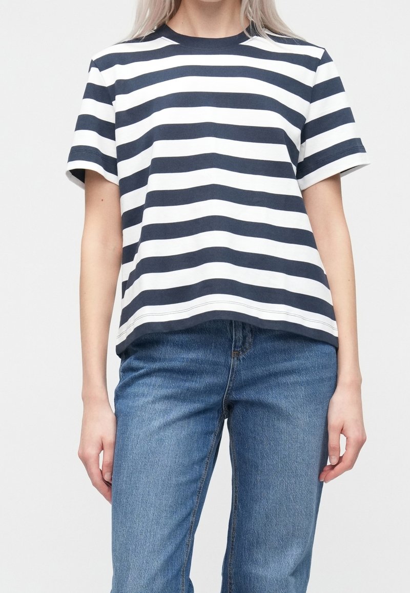 Camiseta de manga corta a rayas azul marino y blancas con cuello redondo; tela de algodón suave; combinada con vaqueros azules de pierna recta.