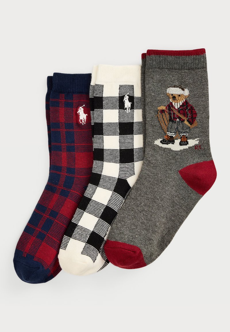 Três pares de meias: uma em padrão quadriculado vermelho e azul marinho, uma em padrão quadriculado preto e branco, e uma cinza com um design de urso. Todas apresentam punhos estriados e acentos contrastantes.