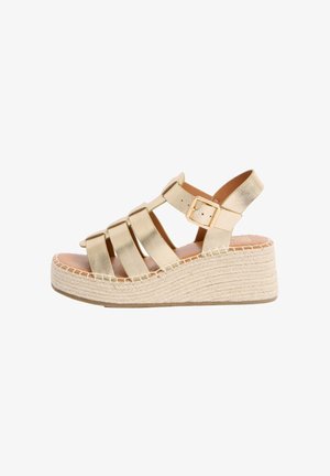 Kultainen remmillä oleva kiilakengän sandaali, jossa säädettävä solki ja kudottu espadrille-tyylinen korokepohja, avoin varvas ja takana kantaremmi.
