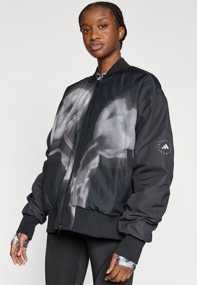 Μαύρο μπουφάν μπόμβερ με γυαλιστερό φινίρισμα, που διαθέτει μεγάλο γκρι γραφικό στο μπροστινό μέρος και ελαστικά μανίκια και τελείωμα. Λογότυπο Adidas στο μανίκι.