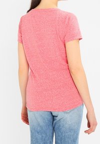 Camiseta de manga corta en tono rosa jaspeado con cuello redondo y dobladillo curvado, combinada con jeans de un azul claro. Textura suave con un patrón sutil.
