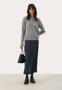 Grau gestrickter Pullover, marineblauer Leopardenmuster-Rock, schwarze Handtasche und klobige schwarze Schuhe. Glatte Texturen und ein lässiger Schnitt.