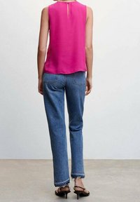 Blouse sans manches fuchsia avec un détail œillet dans le dos, associée à un jean droit bleu clair avec des ourlets usés et des coutures foncées.