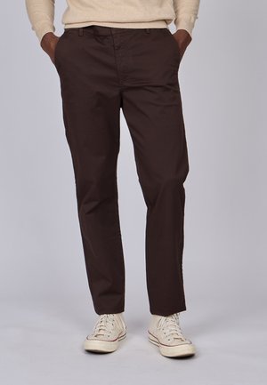 Pantalons en coton marron avec une coupe droite, dotés de poches latérales et d'une taille simple. Portés avec des baskets couleur crème.