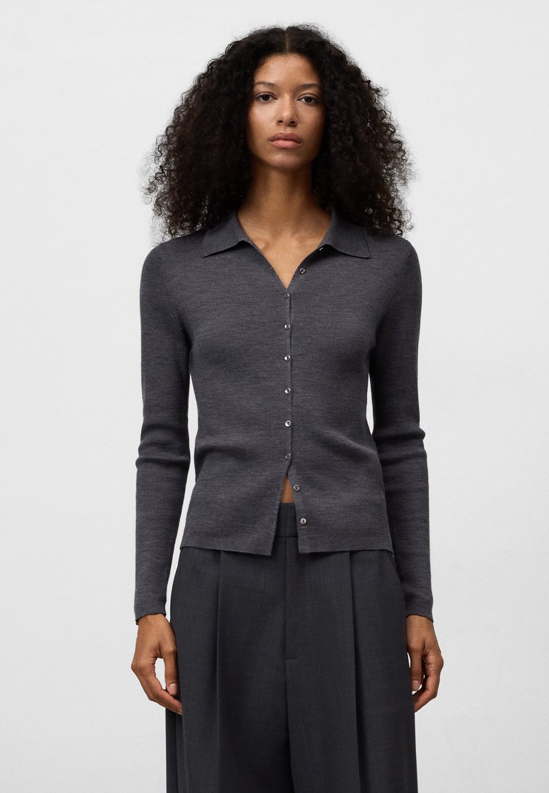 Cardigan grigio a maglia con colletto, chiusura a bottoni e maniche lunghe. Tessuto liscio e design aderente. Abbinato a pantaloni larghi.