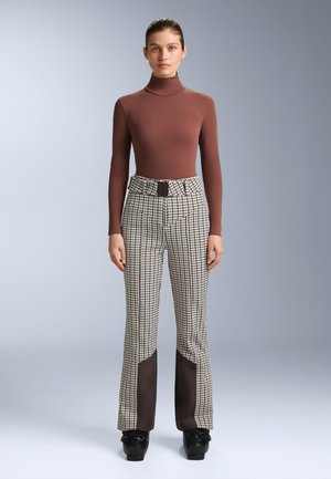 Rjava puli majica z visokim ovratnikom, kombinirana s karirastimi hlačami z visokim pasom, ki imajo na koncih rjavo ploščo in pravokotno sponko za pas.