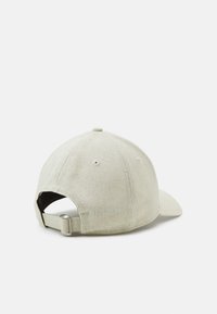 Casquette de baseball en coton beige avec un bord incurvé, sangle ajustable à l'arrière et perforations de ventilation sur le dessus. Fini en tissu texturé.