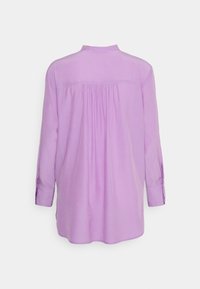 Blouse lilas à manches longues avec des plis froncés sous la fausse patte au dos, des poignets boutonnés et un ourlet droit.