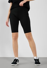 Shorts de vélo noirs côtelés, taille haute, coupe au genou, avec une ceinture élastique, associés à des baskets noires et un haut noir décontracté.