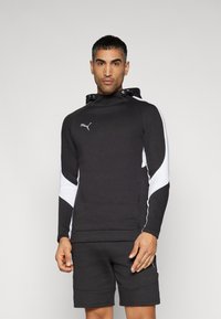 Zwarte sweatshirt met witte accenten, capuchon en logo. Soepele stof, aansluitend ontwerp en kangoeroezak. Gecombineerd met zwarte shorts.