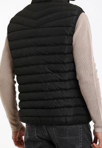 Schwarze Steppweste mit einem Zickzack-Quiltmuster, aus Nylon gefertigt, mit hohem Kragen und Schulternahtdetails.