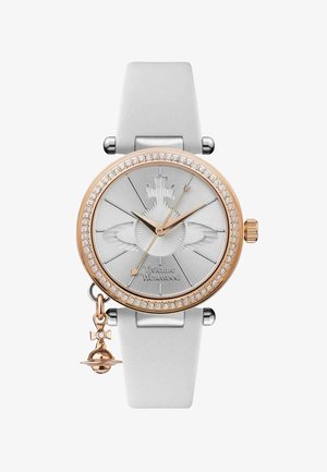 Montre argentée avec un cadran rond, des accents en or rose, un bracelet en silicone blanc et des embellissements en cristal. Elle comprend un charme avec une petite cloche.