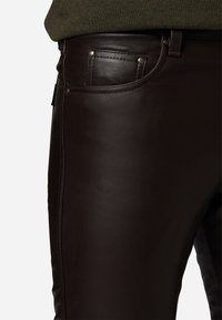 Donkerbruine leren broek met een gladde textuur, voorzien van een voorkleurvak met metalen accenten en zichtbare stiksels langs de zijnaad.