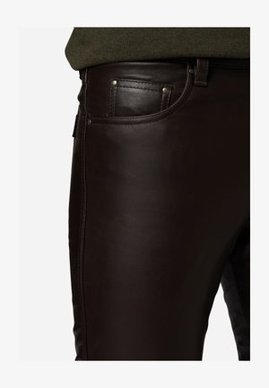 Dunkelbraune Lederhosen mit glatter Textur, ausgestattet mit einer Vordertasche mit Metallelementen und sichtbaren Nähten entlang der Seitennaht.