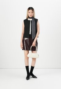 Gilet a righe nere, top bianco, gonna mini in pelle borgogna, foulard a pois, borsa bianca, calzini neri e décolleté appuntiti.