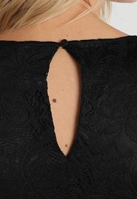 Black lace top featuring a keyhole back design with a button closure. Textured floral pattern and smooth fabric evident in the design.