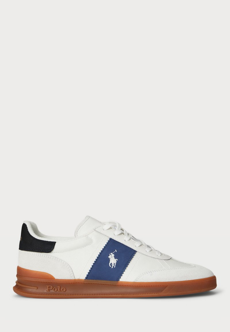 Sapatilha branca com um painel de destaque azul e calcanhar preto. Apresenta um logótipo branco, fecho com atacadores e uma sola de borracha castanha. Material suave.