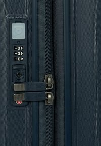 Dettaglio di una valigia rigida blu navy che presenta doppie cerniere, lucchetto TSA e tessuto testurizzato con un motivo sottile. Design compatto e funzionale.