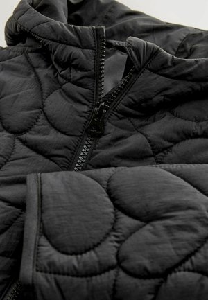 Juodas quilted švarkas su aukštu kaklu, užtrauktuku ir tekstūruotu audiniu su apvaliais raštais. Minkšta ir lengva medžiaga.