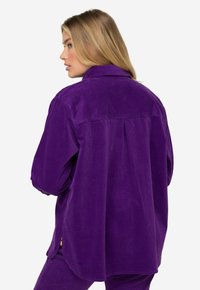 Violetti corduroy-paita kauluksella, näkyvällä pystyribbi-tuntumalla, rento istuvuus ja sivuhalkiot mukavuutta ja liikkumisen helpottamiseksi.