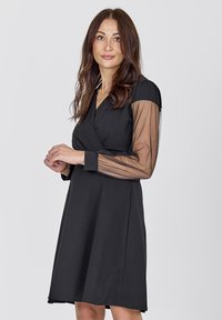 Black wrap dress with a flared skirt and long sheer mesh sleeves, featuring a deep V-neckline and smooth fabric texture.