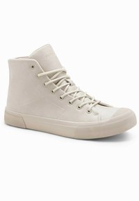 Zapatillas altas de ante beige claro. Sus características incluyen cordones planos, una puntera de goma y una suela texturizada con acentos mínimos.