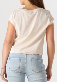 Lichtbeige t-shirt met korte mouwen en een ronde halslijn, gecombineerd met strakke lichte denim jeans met twee achterzakken.