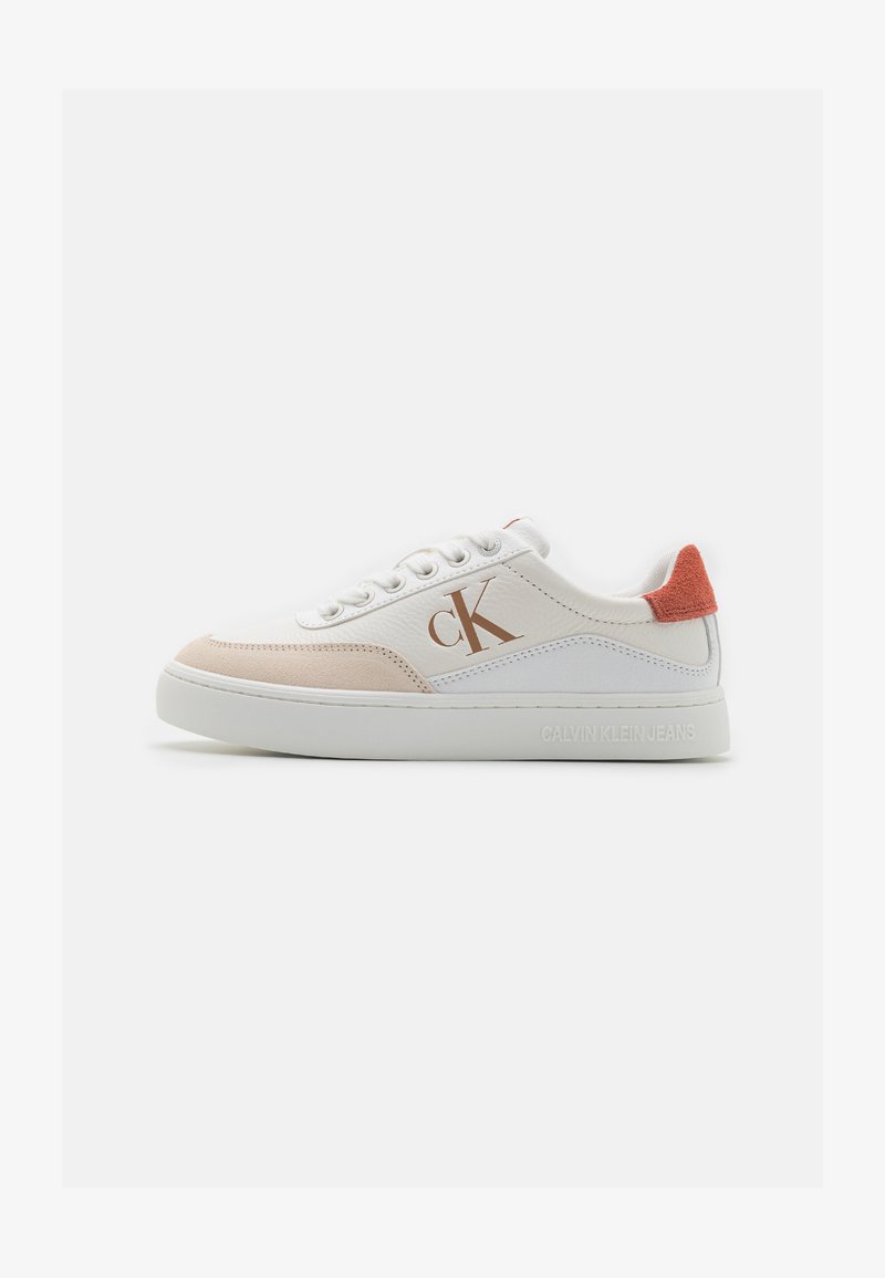 Zapatilla blanca con acentos de ante beige y naranja. Presenta una puntera redonda, suela plana y un logotipo decorativo "CK" en el lateral.